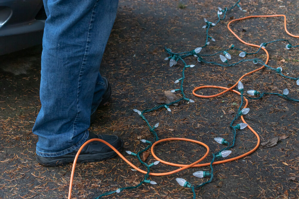 Man standing by string of Christmas lights on ground with orange power cord alongside.