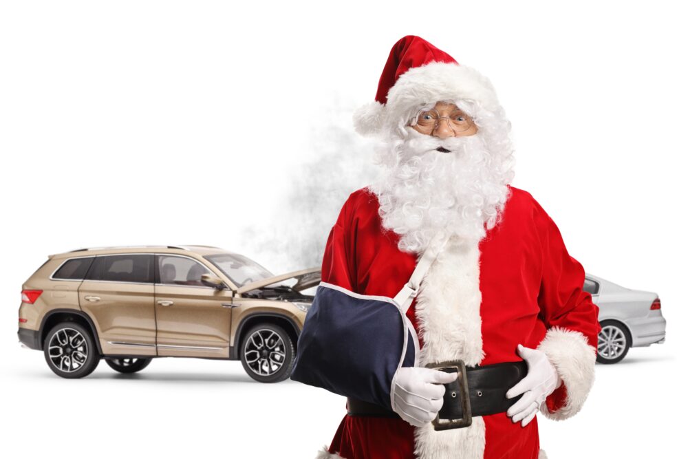 Santa in an arm cast standing in front of a car collision. Smoke emerging from crumpled car hood.
